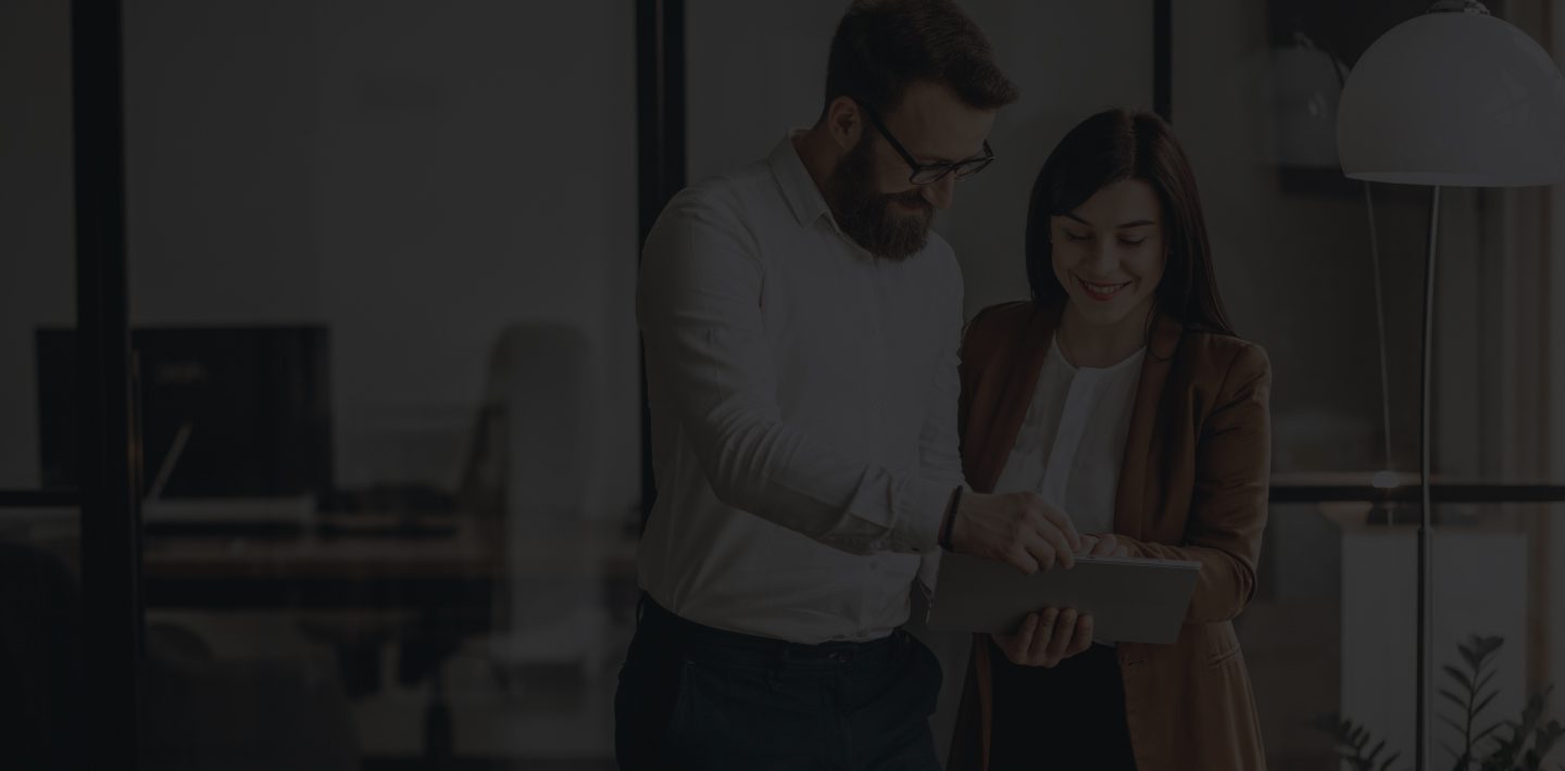 Two Individuals Collaborating, Looking at a Tablet in a Modern, Well-Lit Office Environment.