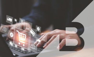 A Person Using a Laptop With Ecommerce-Related Graphic Icons Floating Above the Keyboard Along with the Bigcommerce Logo.