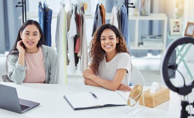 Two Girls Seated at a Table With a Laptop and a Ring Light on a Tripod Stand.