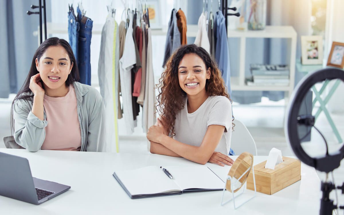 Two Girls Seated at a Table With a Laptop and a Ring Light on a Tripod Stand.