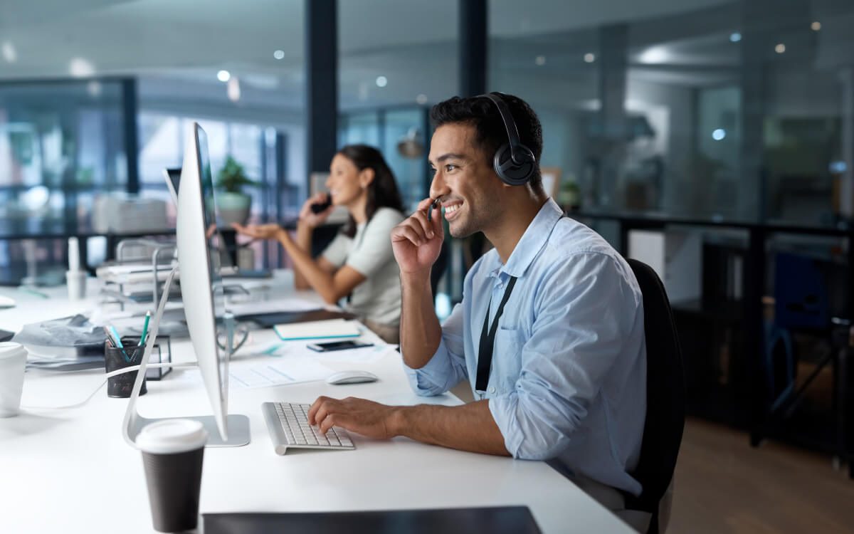 A Man and Woman Working as Support Professionals in a Modern Office Environment Equipped With Computers and Headsets.