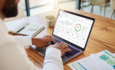 A Person Analyzing Data on a Laptop at a Wooden Desk.