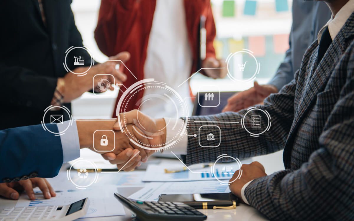 Two Professionals Shaking Hands Over a Table With Digital Icons Floating Around Them.