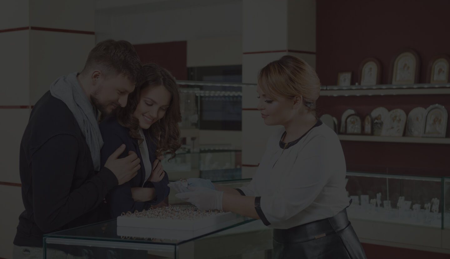 A Couple Interacting With a Salesperson at a Jewelry Store, Examining Various Pieces Displayed on the Counter, With Shelves of Additional Items in the Background.