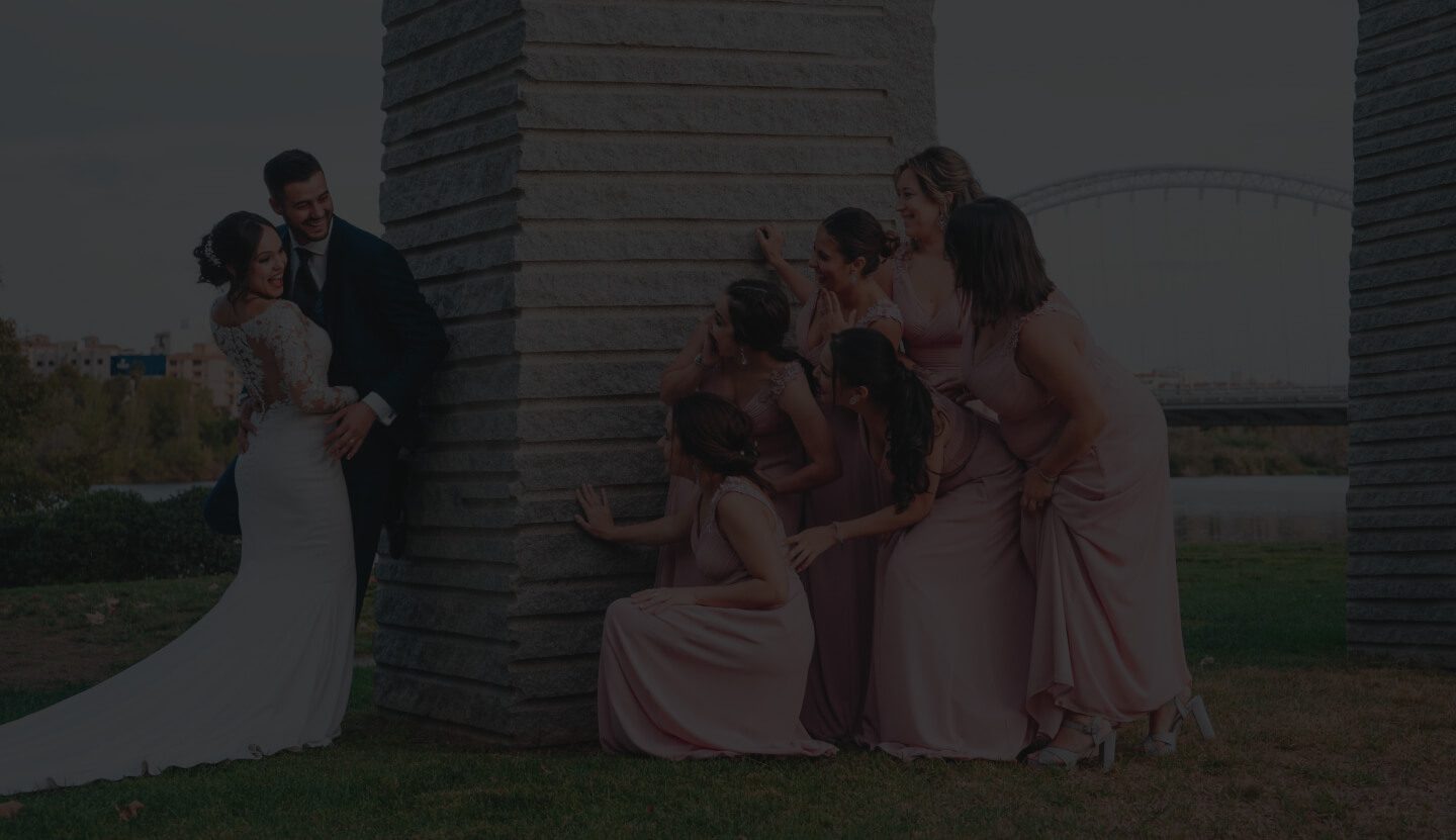 A Wedding Scene With the Bride and Groom Standing Near a Stone Pillar on the Left and a Group of Women Gathered Around It on the Right.