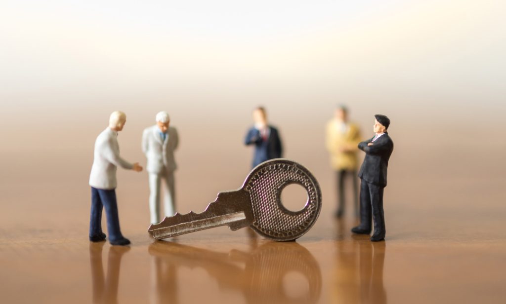 A large key lies on a surface surrounded by miniature figurines of businesspeople.
