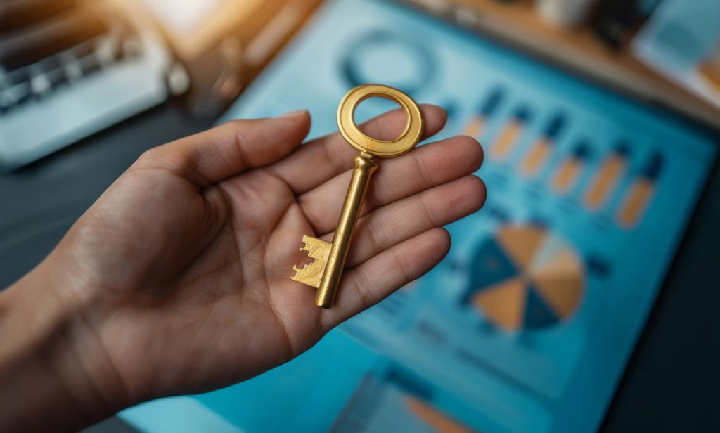 A hand holding a golden key over business charts, symbolizing eCommerce solutions for B2B.