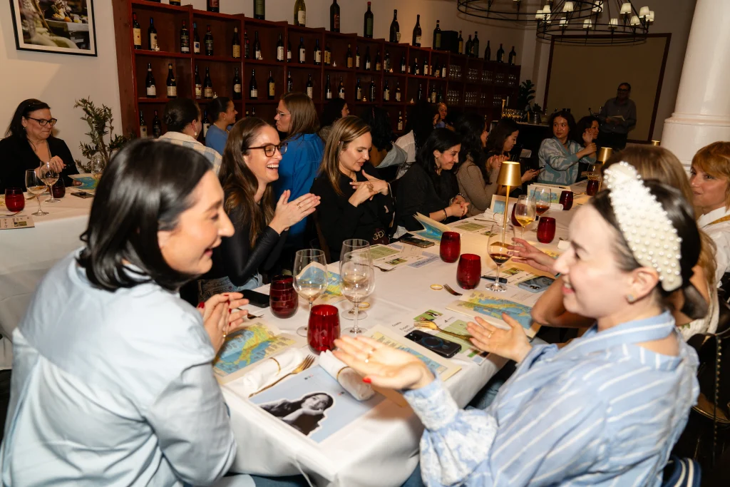 Guests seated around a long, elegant dinner table laugh and chat at the &ldquo;How She Got Here&rdquo; dinner event.
