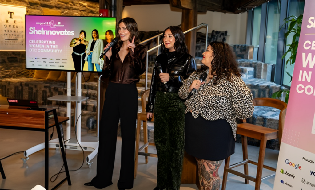 Nicole Harvey, center, speaks at a SheInnovates event celebrating women in the DTC community, standing with two other women holding microphones.