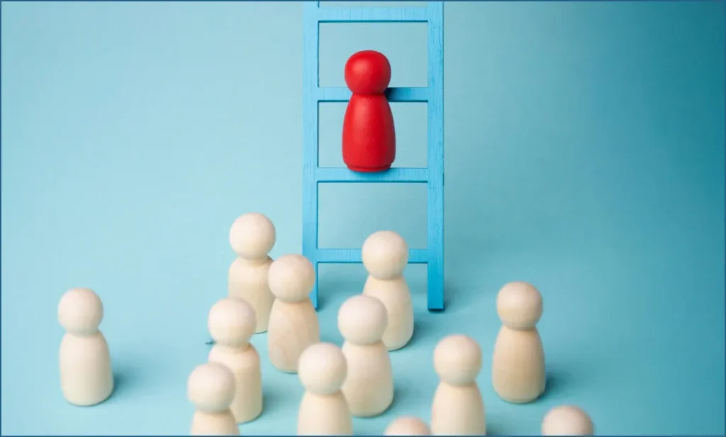  A Red Wooden Figure Standing on a Blue Ladder Above a Group of Beige Wooden Figures, Symbolizing Resilience and Representation.