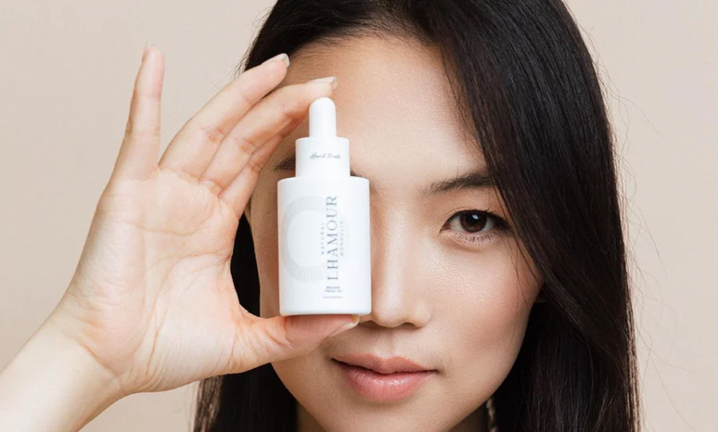 A model holding up a white Lhamour skincare serum bottle in front of her face.
