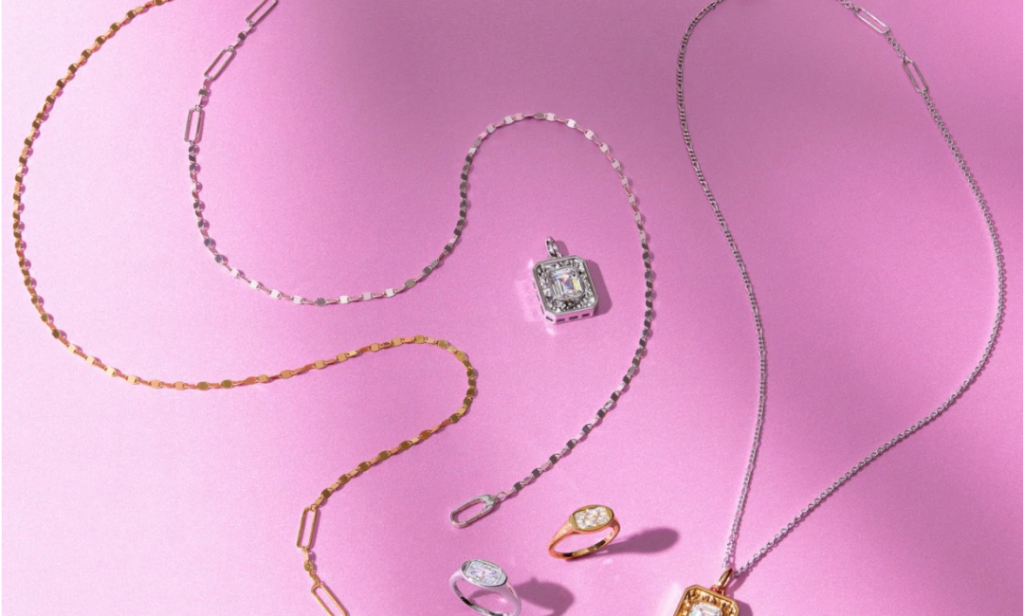 A flat lay of various Claspe jewelry pieces on a vibrant pink background.