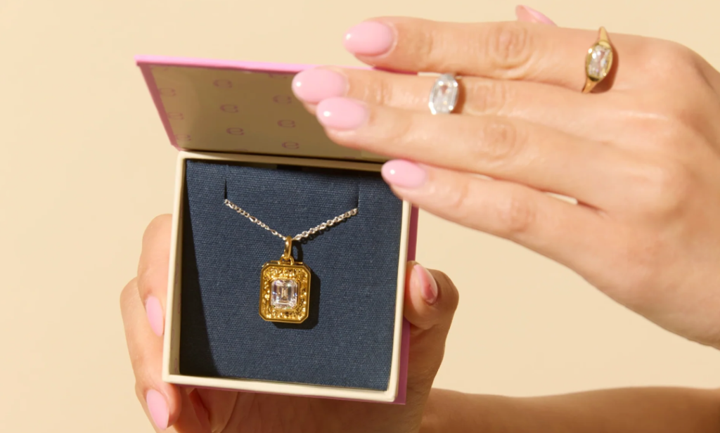 Hand holding a box with a gold pendant necklace inside